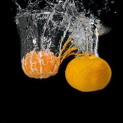 Image showing Fresh tangerines dropped into water with bubbles on black