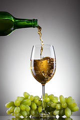 Image showing White wine pouring into glass from bottle with green grape