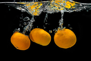 Image showing Fresh tangerines dropped into water with bubbles on black