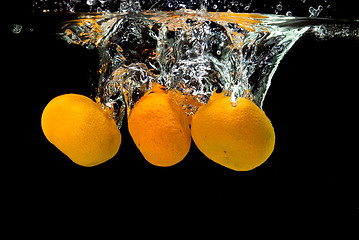 Image showing Fresh tangerines dropped into water with bubbles on black