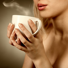 Image showing woman holding hot cup and blowing on it