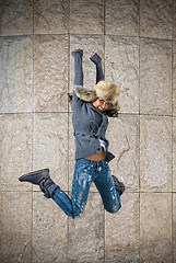 Image showing young woman jumping in fur hat against the wall