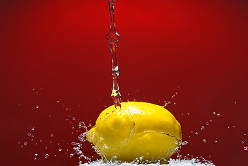 Image showing Fresh lemon and water splash on red