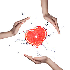 Image showing Heart of grapefruit with water splash and human hands on white