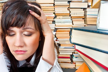 Image showing College girl holding her head against many books