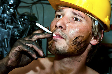 Image showing Worker covered in oil smoking