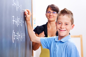 Image showing Boy standing on chalkboard in front of teacher