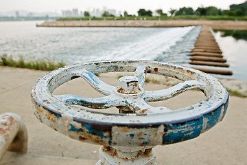 Image showing White and blue rusty industrial faucet wheel on river blurry bac