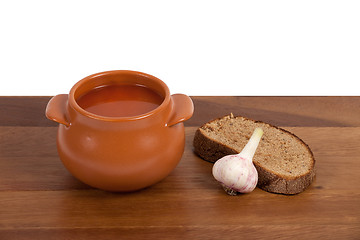 Image showing Borsch in ceramic pot with bread and garlic on wooden table