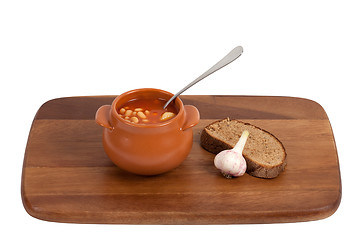 Image showing Soup in clay pot with bread and garlic on wooden kitchen board.