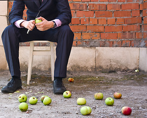 Image showing Businessman cleaning apples sitting on a stool