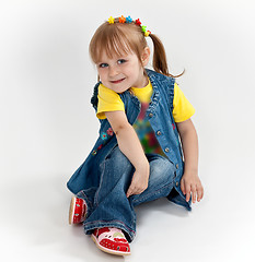 Image showing little girl in jeans and sandals is sitting on the floor