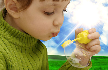 Image showing The girl inflating soap bubbles on a meadow