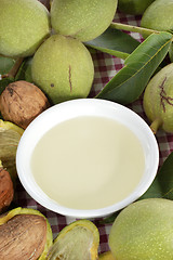 Image showing fresh walnut oil in a bowl with harvested unopened green walnuts