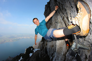 Image showing Young man climbing steep wall above lake