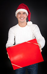 Image showing Smiling man in Santa hat gives a red box in the studio