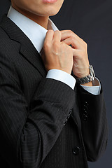 Image showing young man adjusting his suit on a black background 