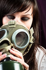 Image showing Beautiful girl is holding an old gasmask against dark background