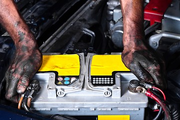 Image showing Engineer with oil on his hands holding a car battery tight