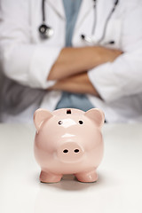 Image showing Doctor with Folded Arms Behind Piggy Bank