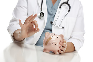 Image showing Doctor Gives Okay Sign Behind Piggy Bank