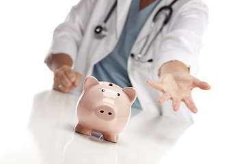 Image showing Demanding Doctor Reaches Palm Out Behind Piggy Bank