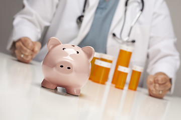 Image showing Doctor with Fists on Table Behind Bottle and Piggy Bank