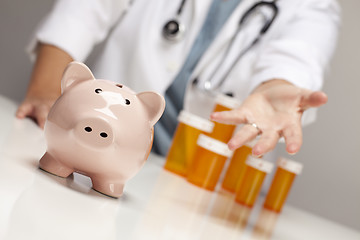 Image showing Doctor Reaches Palm Out Behind Medicine Bottles and Piggy Bank