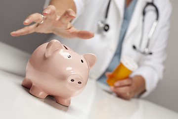 Image showing Doctor with Medicine Bottles Reaches for Piggy Bank.