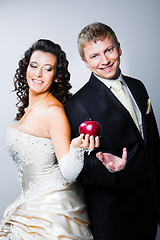 Image showing just married bride tempting smiling groom by red apple