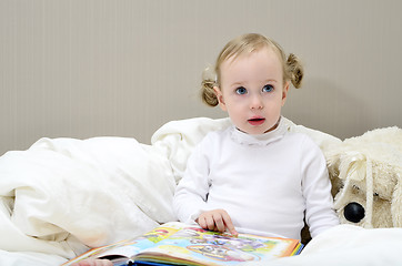 Image showing little girl sitting on the bed and reading a book
