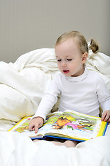 Image showing little girl sitting on the bed and reading a book