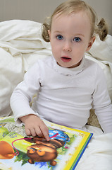 Image showing little girl sitting on the bed and reading a book