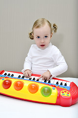 Image showing little girl sitting on the bed and plays on a children's keyboard