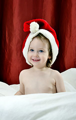 Image showing little girl in a Christmas red hat sitting on a bed