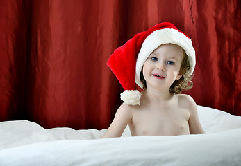 Image showing little girl in a Christmas red hat sitting on a bed