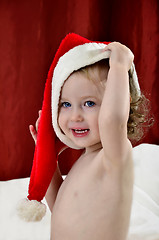 Image showing little girl in a Christmas red hat sitting on a bed