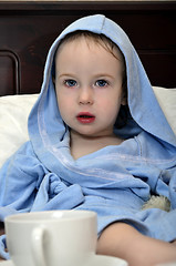 Image showing little girl in a blue robe resting on the bed after a shower with a cup of tea