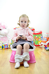 Image showing little girl sitting on the potty with a remote control (or mobile phone) in hand