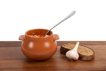 Image showing Borsch in clay pot with bread and garlic on wooden table