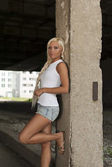 Image showing athletic girl in denim shorts and white T-shirt standing at the pillar