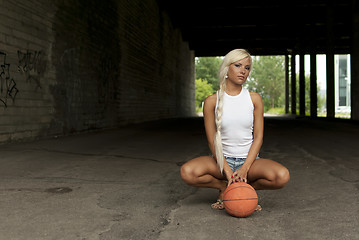 Image showing Beautiful blonde girl is sitting with basketball on the street