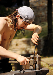 Image showing Young blacksmith hammering hot iron on anvil