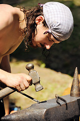 Image showing Young blacksmith hammering hot iron on anvil