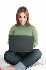 Image showing Excited girl in jeans with laptop sitting on her bed isolated 