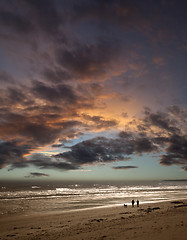 Image showing Couple walking dog on beach at sunset