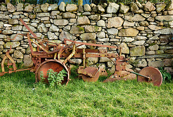 Image showing Old rusty plow in shadow of stone wall