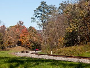 Image showing Pair of cyclists ride along railway