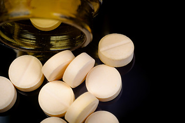 Image showing Medical pills out of their bottle on black background