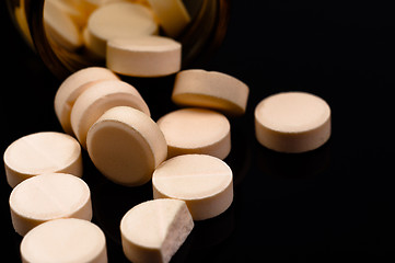Image showing Medical pills out of their bottle on black background
